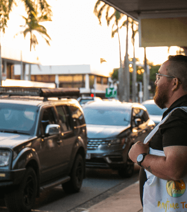 Tourist wearing an Anytime Tours vest, standing on a street with cars and palm trees, representing the local expertise on a Mackay private tour.